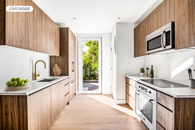 kitchen featuring modern cabinets, a sink, light wood-style floors, stainless steel oven, and decorative backsplash