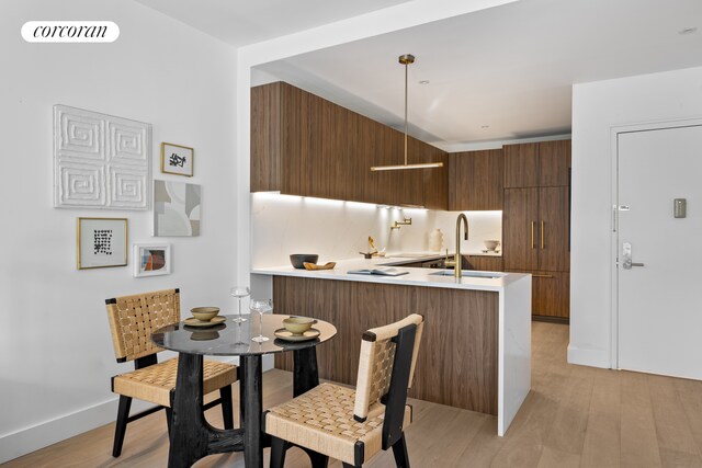 kitchen with a sink, modern cabinets, light wood-type flooring, a peninsula, and light countertops