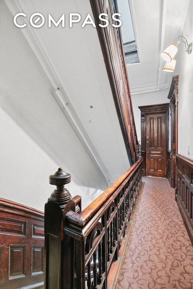 hallway featuring light colored carpet, a wainscoted wall, and a decorative wall