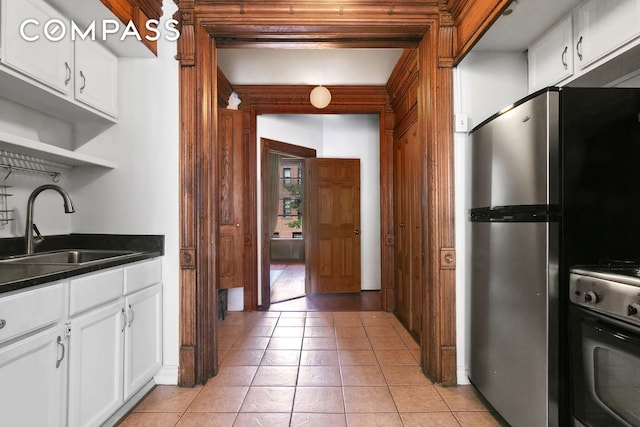 kitchen with dark countertops, stove, freestanding refrigerator, white cabinetry, and a sink