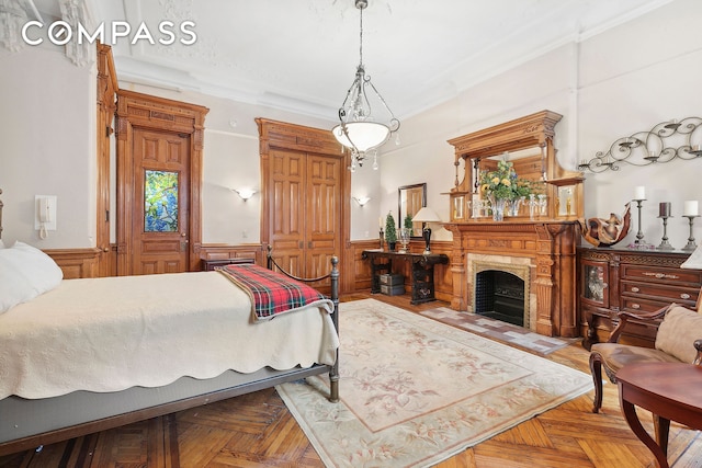 bedroom with a wainscoted wall, a fireplace with flush hearth, and ornamental molding