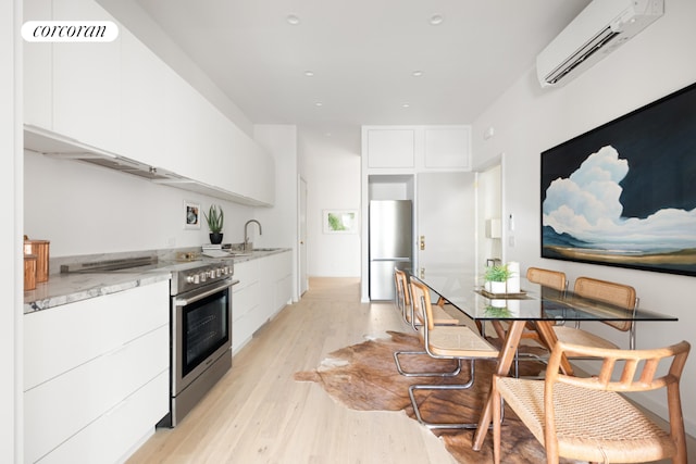 kitchen featuring light stone countertops, white cabinetry, an AC wall unit, light wood-type flooring, and stainless steel appliances