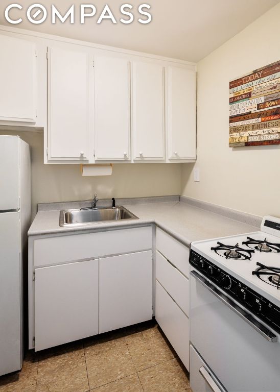 kitchen featuring light tile patterned floors, white cabinetry, sink, and white appliances