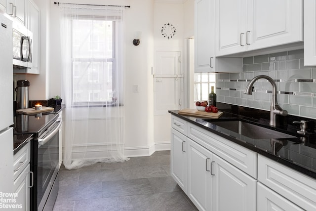 kitchen featuring dark countertops, appliances with stainless steel finishes, a sink, white cabinetry, and backsplash