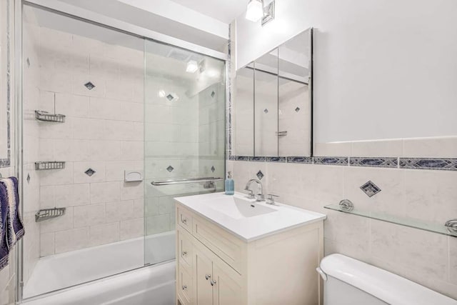 full bathroom featuring vanity, bath / shower combo with glass door, tile walls, and toilet