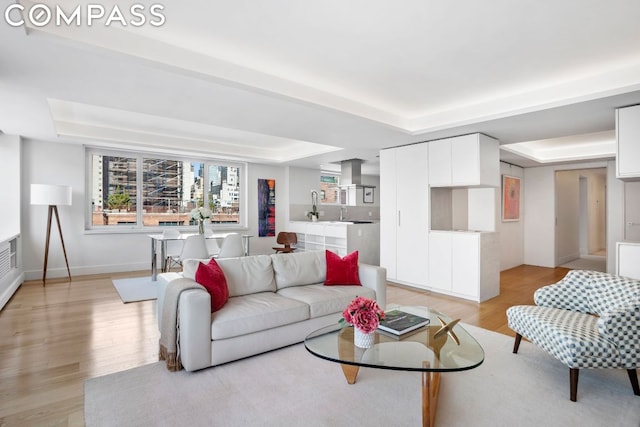 living room featuring light wood-type flooring, a tray ceiling, and sink