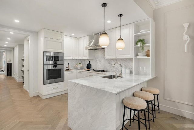 kitchen with light parquet floors, white cabinetry, wall chimney range hood, and kitchen peninsula