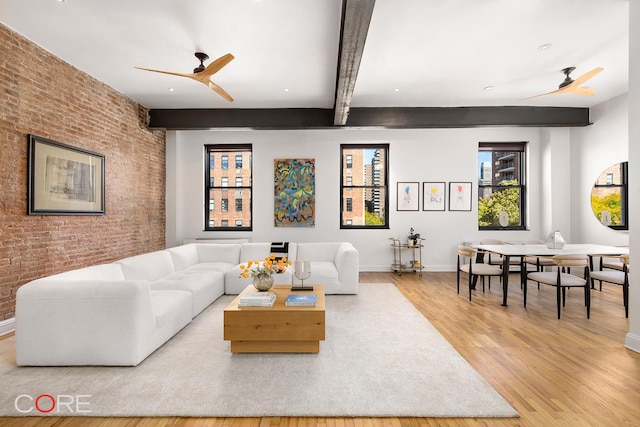 living area with brick wall, a ceiling fan, wood finished floors, and beamed ceiling