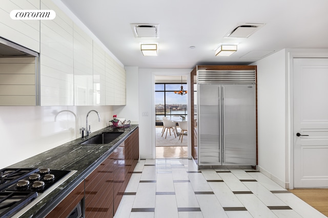 kitchen featuring sink, appliances with stainless steel finishes, dark stone counters, and an inviting chandelier