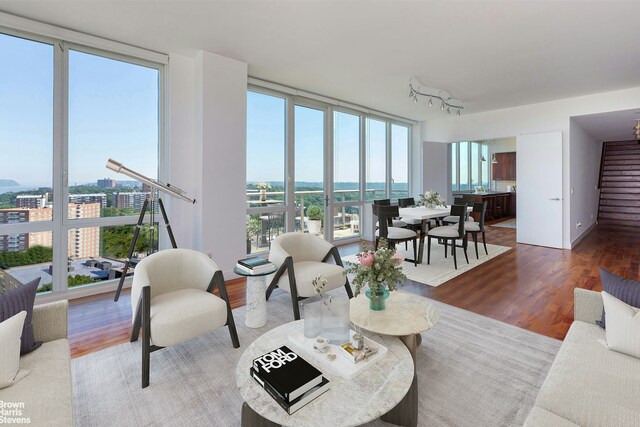 living area with floor to ceiling windows, a city view, wood finished floors, plenty of natural light, and stairs