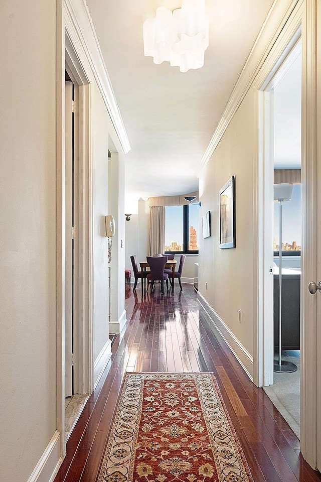 hallway featuring a chandelier, ornamental molding, dark wood-type flooring, and baseboards