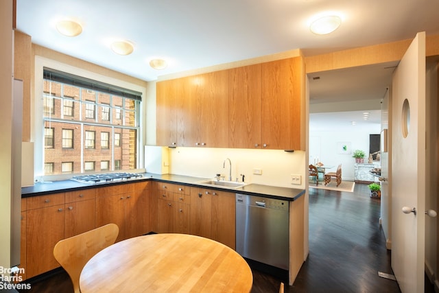 kitchen with stainless steel appliances, a sink, dark wood-style floors, brown cabinetry, and dark countertops