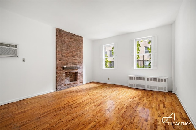 unfurnished living room with a wall unit AC, baseboards, light wood-style flooring, radiator heating unit, and a brick fireplace