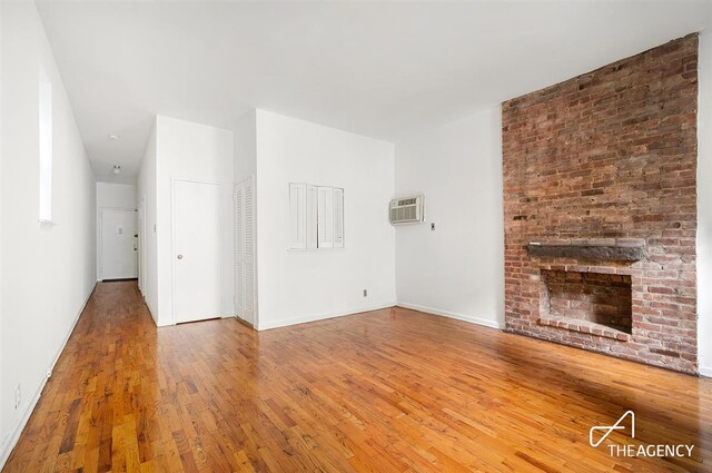 unfurnished living room with hardwood / wood-style flooring, a wall mounted AC, and a fireplace