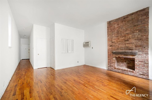 unfurnished living room featuring hardwood / wood-style flooring, an AC wall unit, and a fireplace