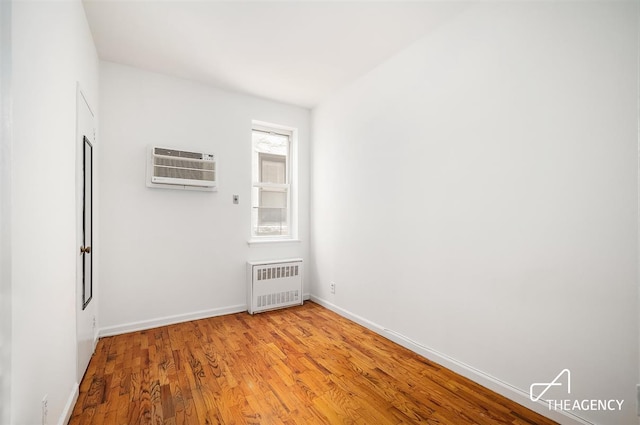 spare room featuring an AC wall unit, light wood-style flooring, radiator heating unit, and baseboards