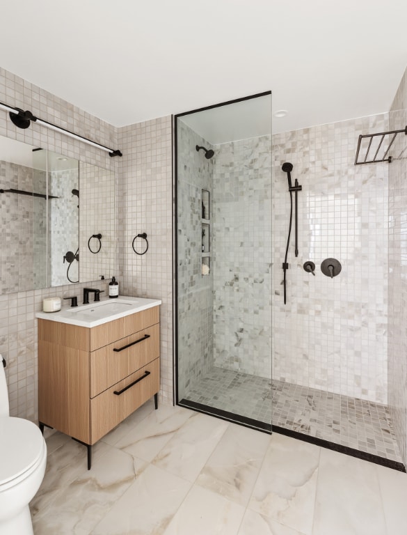 bathroom with a tile shower, tile walls, vanity, and toilet