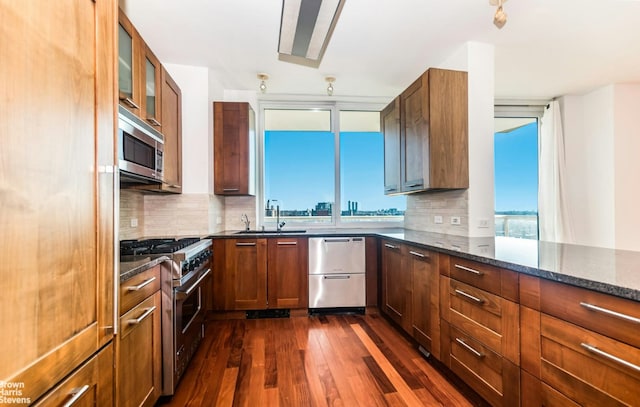 kitchen with appliances with stainless steel finishes, dark stone countertops, backsplash, a wealth of natural light, and dark hardwood / wood-style flooring