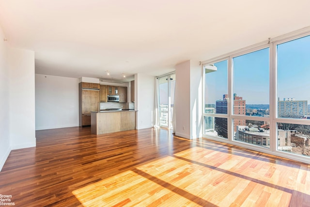 unfurnished living room featuring floor to ceiling windows, dark wood-type flooring, baseboards, and a city view