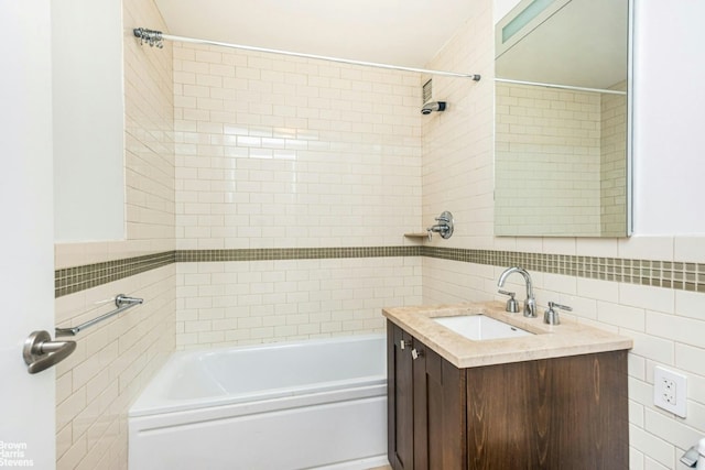 bathroom featuring tiled shower / bath combo, vanity, and tile walls