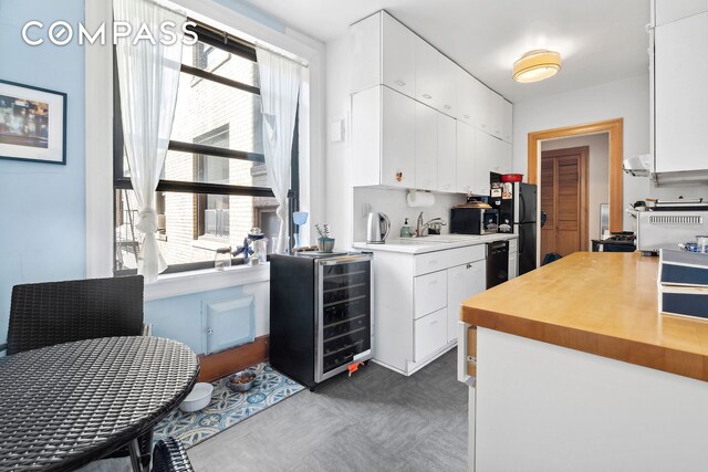 kitchen featuring sink, white cabinetry, beverage cooler, and black appliances