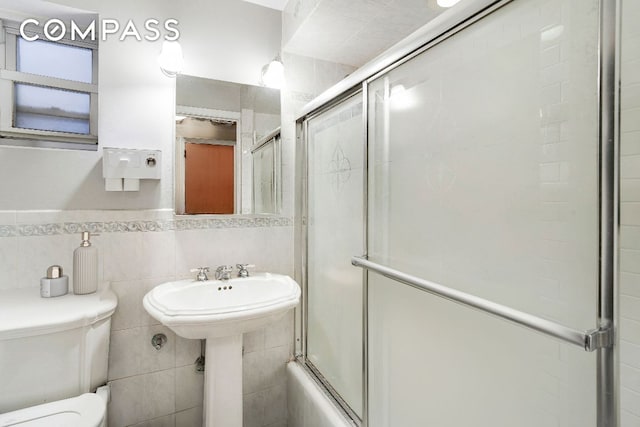 bathroom featuring toilet, combined bath / shower with glass door, and tile walls