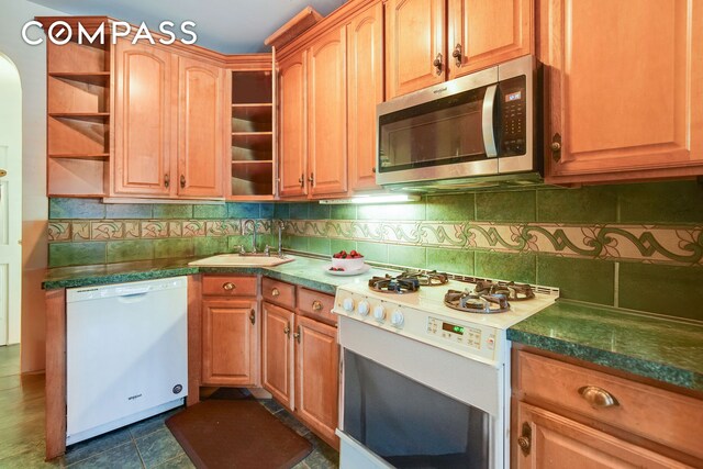 kitchen featuring dark countertops, white appliances, a sink, and backsplash