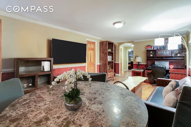 dining room featuring arched walkways, light wood finished floors, and crown molding