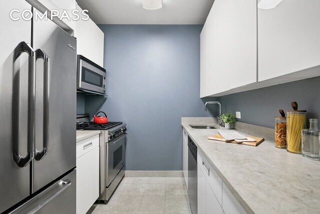 kitchen with stainless steel appliances, sink, light tile patterned floors, and white cabinets