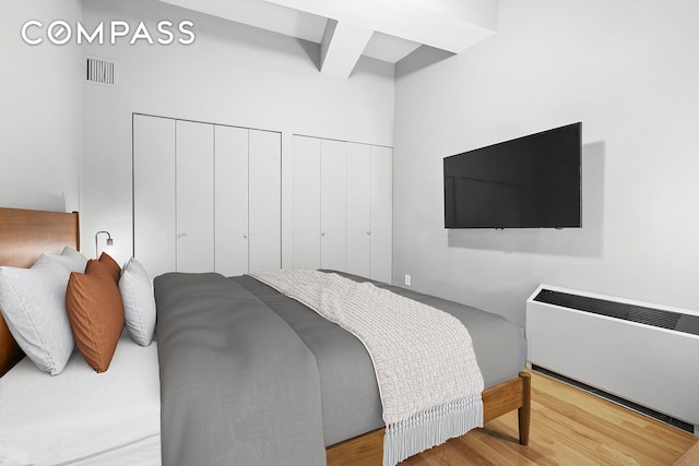 bedroom featuring beamed ceiling, wood finished floors, visible vents, and multiple closets