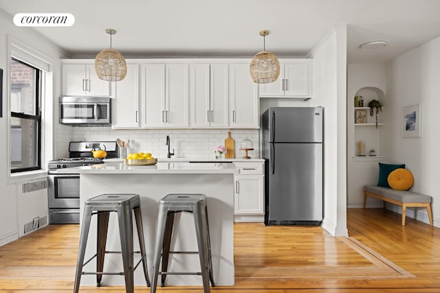 kitchen featuring a breakfast bar, white cabinetry, pendant lighting, stainless steel appliances, and backsplash