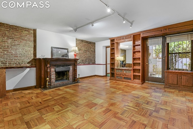 unfurnished living room with light parquet flooring, a fireplace, brick wall, and track lighting