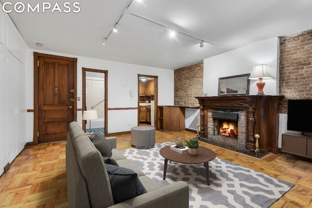 unfurnished living room with light parquet flooring, a fireplace, brick wall, and track lighting