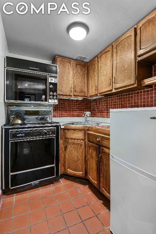 kitchen featuring backsplash, tile patterned floors, sink, white refrigerator, and range