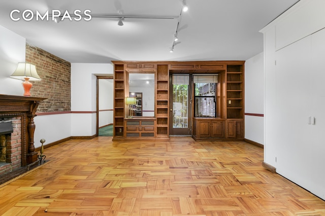 unfurnished living room with a fireplace, rail lighting, and baseboards