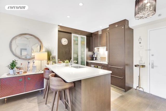 kitchen with sink, a breakfast bar area, light hardwood / wood-style floors, dark brown cabinets, and a center island with sink