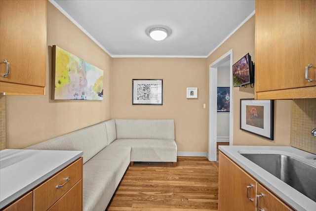 unfurnished living room featuring a sink, crown molding, light wood finished floors, and baseboards
