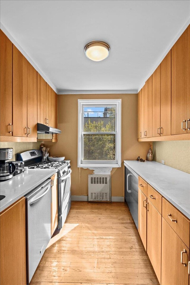 kitchen featuring appliances with stainless steel finishes, radiator heating unit, light wood-style floors, tasteful backsplash, and crown molding
