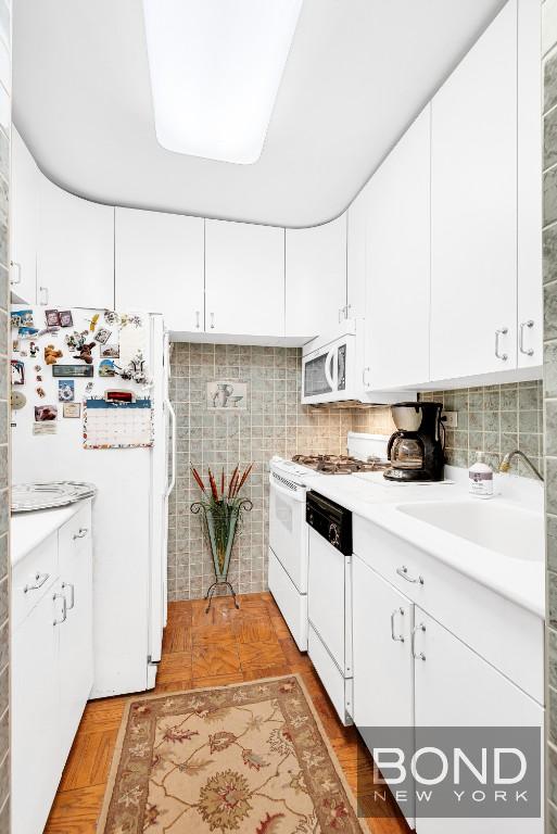 kitchen featuring white cabinetry, sink, backsplash, and white appliances