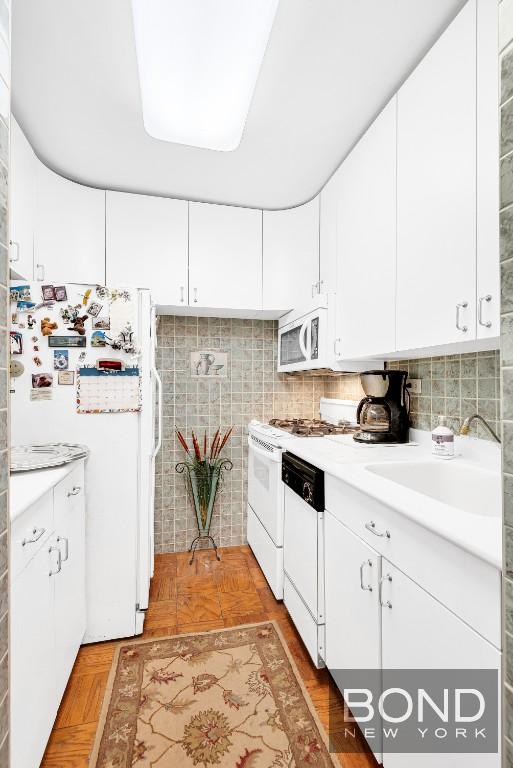 kitchen with light countertops, a sink, white cabinets, and white appliances