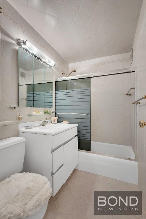 full bath with tile patterned flooring, tile walls, toilet, bathing tub / shower combination, and vanity