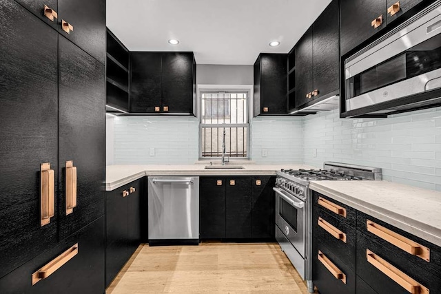 kitchen with appliances with stainless steel finishes, backsplash, light hardwood / wood-style flooring, light stone counters, and sink