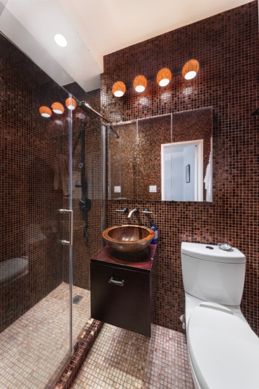 bathroom featuring toilet, a shower with door, tile patterned flooring, tile walls, and vanity