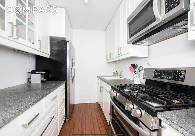 kitchen with dark wood-style flooring, a sink, white cabinets, appliances with stainless steel finishes, and glass insert cabinets