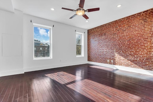 unfurnished room featuring ceiling fan, dark wood-type flooring, and brick wall