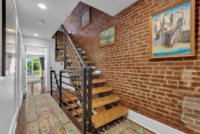stairway with wood finished floors, brick wall, recessed lighting, and baseboards