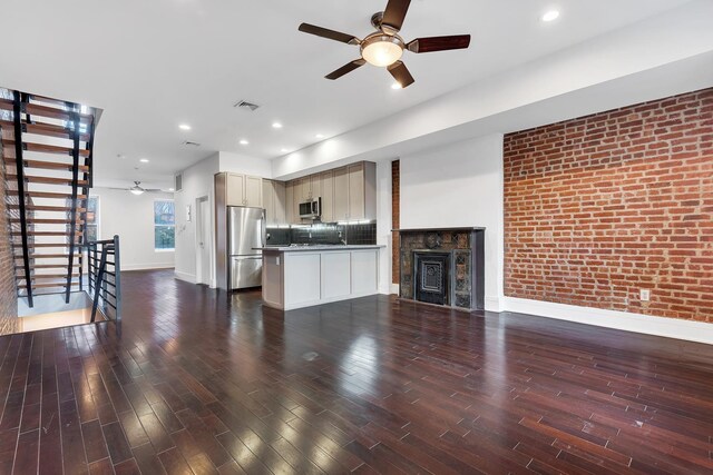 unfurnished living room with visible vents, baseboards, brick wall, wood finished floors, and a ceiling fan
