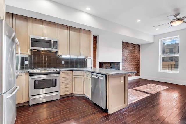 kitchen featuring stainless steel appliances, dark wood-style flooring, a peninsula, and a sink