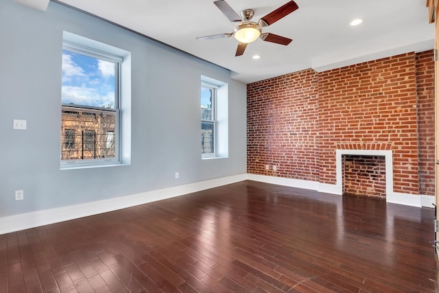 unfurnished living room featuring ceiling fan, brick wall, wood finished floors, and baseboards