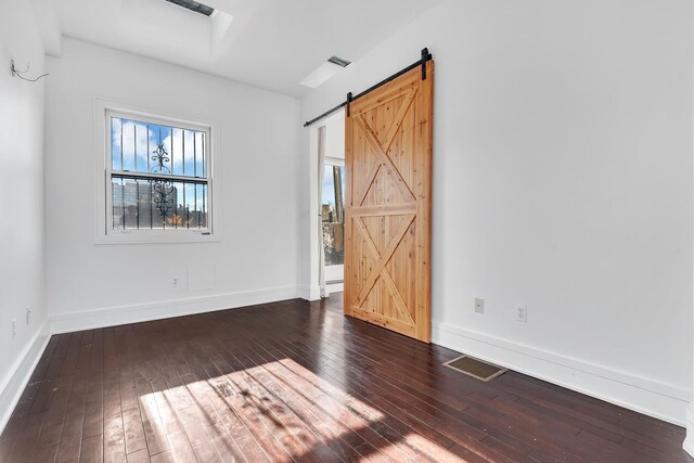 unfurnished bedroom with a barn door, hardwood / wood-style flooring, visible vents, and baseboards